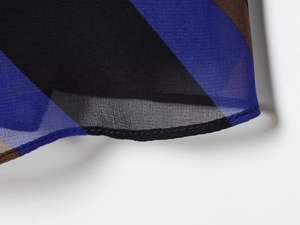 Dettaglio del tessuto chiffon geometrico con motivi blu e marroni e cuciture fini