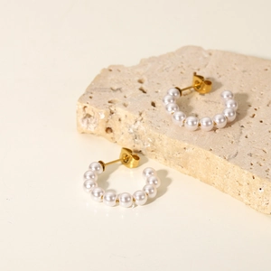 Detail of C-shaped gold hoop earrings with small pearls and butterfly backs on stone decor