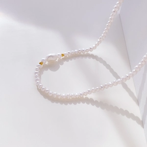 Detail of irregular baroque pearl necklace with golden accent beads on a white surface