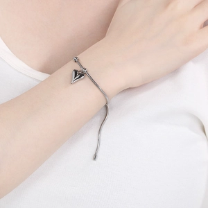 Detail of silver heart charm on a sleek snake chain bracelet with adjustable tail link