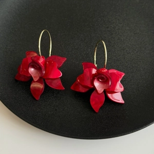 Close-up of red orchid flower resin earrings with golden metal hooks on a black tray