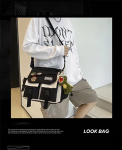 Close-up of black and white messenger bag with buckle closure and green dinosaur charm