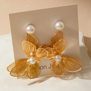 Detailed macro view of large golden filigree butterfly earrings with white pearl accents