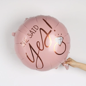 Detailed view of a pink round foil balloon with rose gold She Said Yes text and ring icon