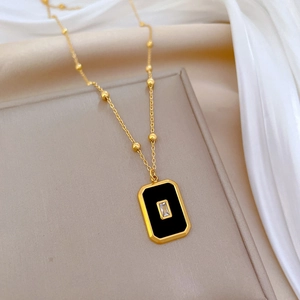 Detailed shot of golden bead chain necklace featuring a black rectangle stone and clear gem