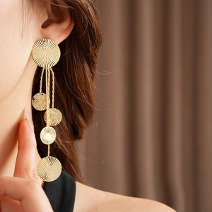 Detail of gold tassel earrings with textured round discs shown on model's ear