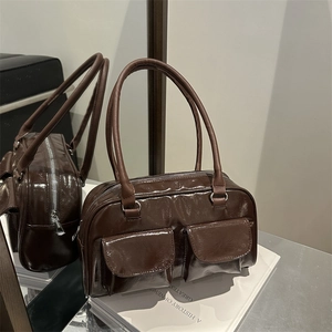 Borsa a spalla in pelle verniciata marrone con doppie tasche e manici su un libro