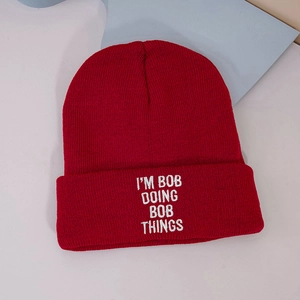 Red knit beanie with I'M BOB DOING BOB THINGS white embroidery text in flat lay view