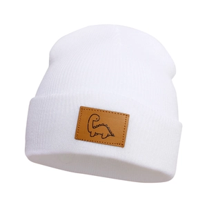 Dettaglio del berretto in maglia bianca per bambini con toppa in pelle e dinosauro