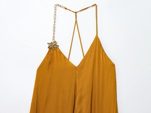 Detail of yellow satin midi dress with golden flower ornaments and metal chain straps