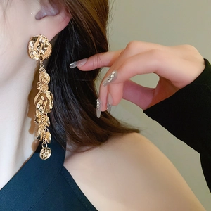 Détail de boucles d'oreilles pendantes dorées avec texture martelée sur le modèle