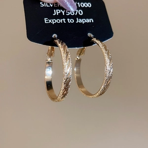 Detail of gold-textured hoop earrings with a frosted finish on a black display card