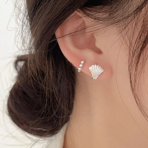 Close-up of minimalist sterling silver shell stud earrings and beaded ear cuff on model
