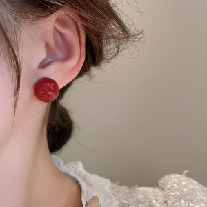 Close-up of elegant red spherical stud earrings with glossy finish on model's ear