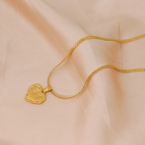 Gold heart pendant necklace with hammered texture and fine snake chain on silk backdrop