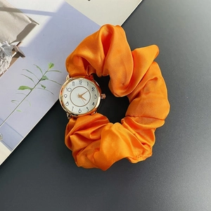 Creative orange silk scrunchie watch with a golden round dial on a designer magazine