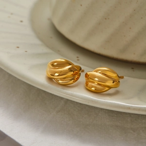 Detailed close-up of golden twisted texture earrings on a white ceramic plate