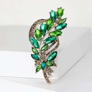 Close-up of elegant leaf brooch with green marquise crystals on a white pedestal