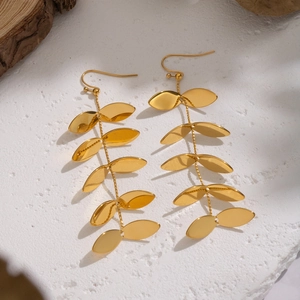 Macro detail of gold leaf tassel earrings on natural wood and stone textures