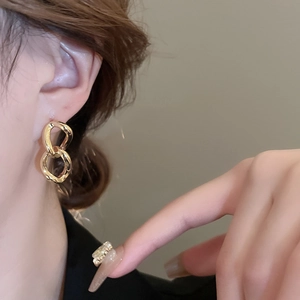 Elegant gold-plated geometric link earrings worn by a model in a close-up studio shot