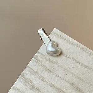 Detail of silver alloy hair clip with heart-shaped white pearl on natural fiber card