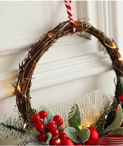 Detail of Christmas wreath with red berries, frosted leaves, and warm LED fairy lights