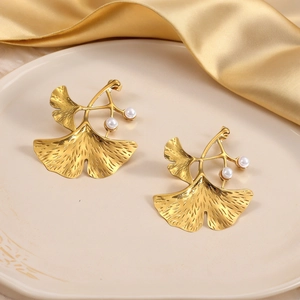 Golden ginkgo leaf earrings with white pearls on elegant silk fabric background