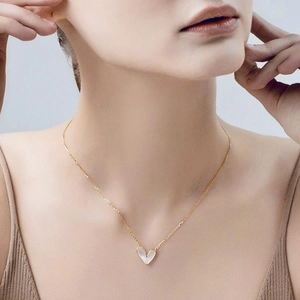 Detail of a gold heart pendant necklace featuring an asymmetric white shell on a model