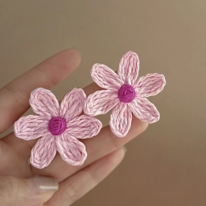 Detail of handmade woven pink floral earrings with purple center and silver needles