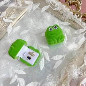 Close-up of cute green velvet frog-shaped jewelry boxes with gold rings on lace background