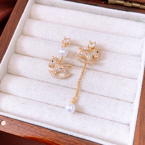 Close-up of asymmetrical 18k gold plated rocking horse earrings with pearls and zircons