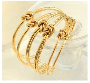 Dettaglio di quattro bracciali rigidi dorati con nodi e texture metalliche a treccia