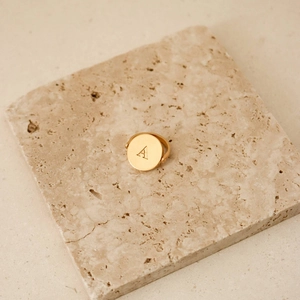 Gold stainless steel signet ring with initial A on beige travertine stone pedestal
