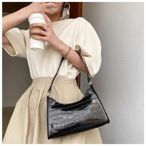 Detail of black faux leather shoulder bag featuring crocodile pattern and gold hardware