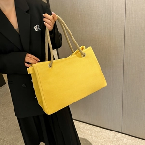 Yellow canvas tote bag with knotted handles carried by model in black blazer