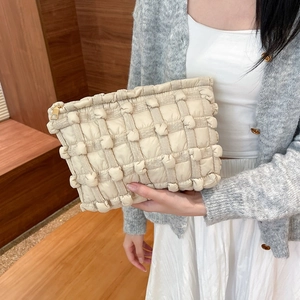 Close-up of beige quilted canvas clutch with bubble texture and gold zipper detail