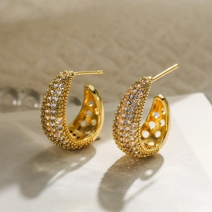 Macro shot of gold-plated C-shaped earrings with micro-set zircon and grainy metal texture