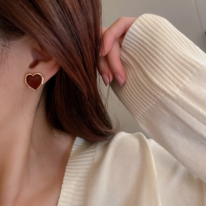 Detail of red enamel heart earring with gold metal trim worn by a model in warm light