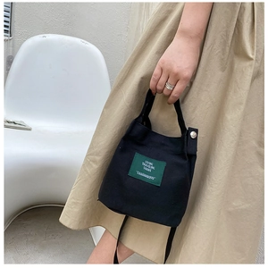 Detail of black canvas bucket bag with green woven label and metal snap button closure