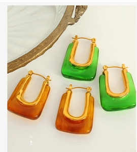 Close-up of geometric U-shaped resin earrings in green and amber with gold-tone hooks
