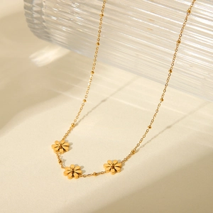 Minimalist gold daisy flower stainless steel necklace with small beads on a beige surface
