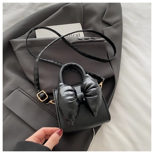 Detail of a black PU leather handbag featuring a large stylish bow on a grey blazer background
