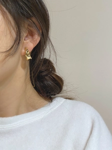 Close-up of golden irregular liquid metal earrings worn by a model in a minimalist style