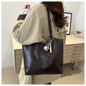 Detail view of dark brown leather tote bag with a baseball charm and crossbody strap