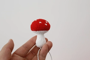Detailed view of a handmade crochet mushroom bag charm held in hand for size comparison