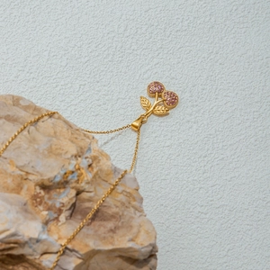 Close-up of a gold cherry necklace with pink zircons resting on a textured rock surface