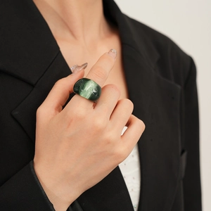Detail view of a wide dark green resin ring with cat-eye effect worn on index finger
