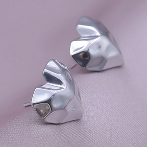 Macro view of silver heart stud earrings with hammered metal texture on pink fabric