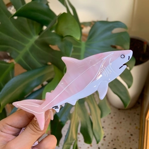 Detailed close-up of a pink and white shark-shaped hair claw clip held over green leaves