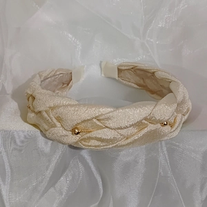 Detail of beige woven headband with golden beads on white silk background